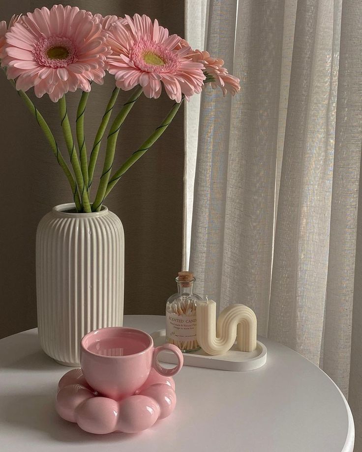 pink flowers in a white vase next to a cup and saucer on a table