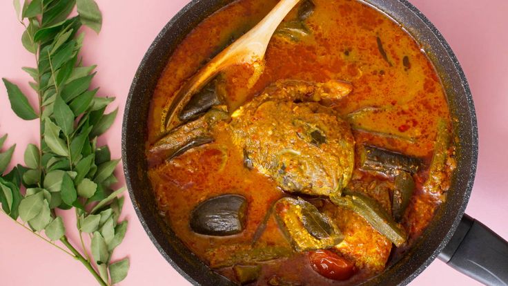 a pot filled with stew and vegetables on top of a pink surface next to green leaves