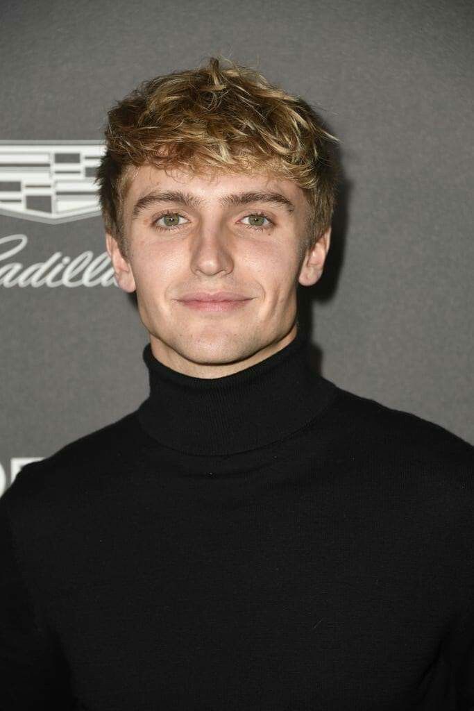 a man with blonde hair wearing a black turtle neck sweater and posing for the camera