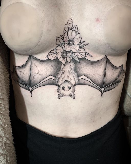 a woman's stomach with a bat tattoo and flowers on the top part of it