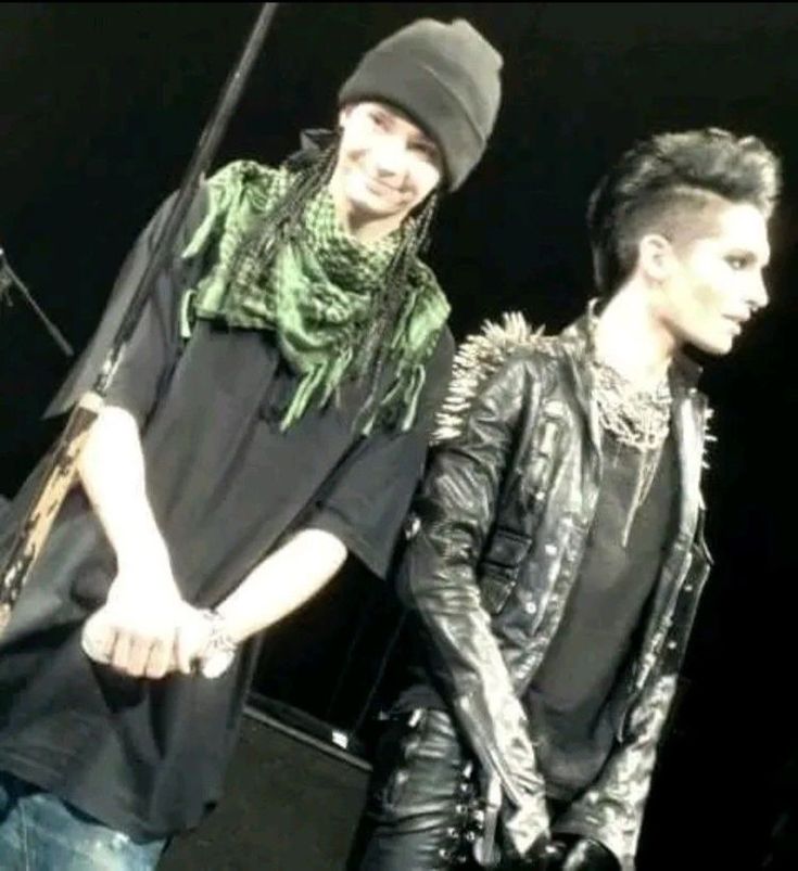 two men standing next to each other on stage wearing black leather jackets and scarfs