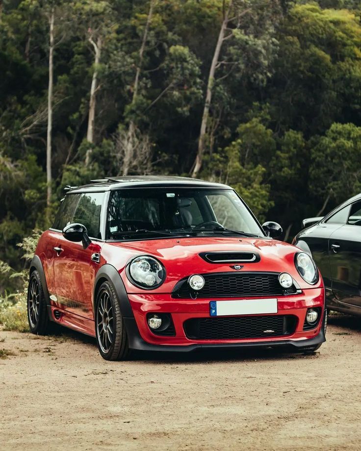 two cars parked next to each other on a dirt road in front of some trees