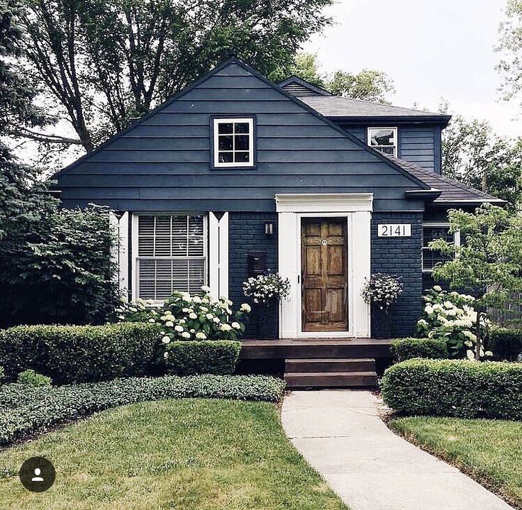 a blue house with white trim and flowers on the front door is surrounded by hedges