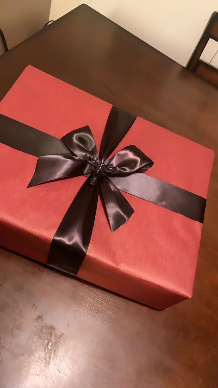 a red gift box with black ribbon and bow sitting on top of a wooden table