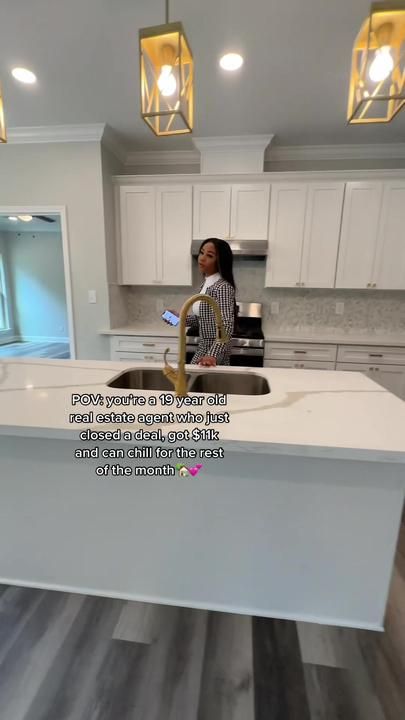 a woman is standing in the middle of a kitchen with an island counter top and white cabinets