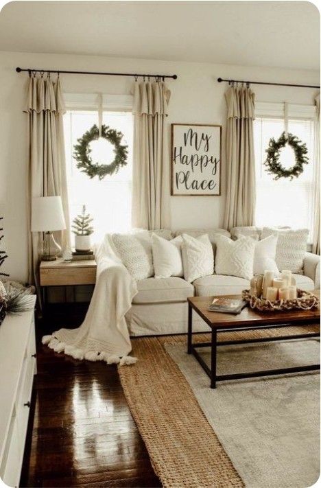 a living room filled with white furniture and christmas wreaths on the window sill