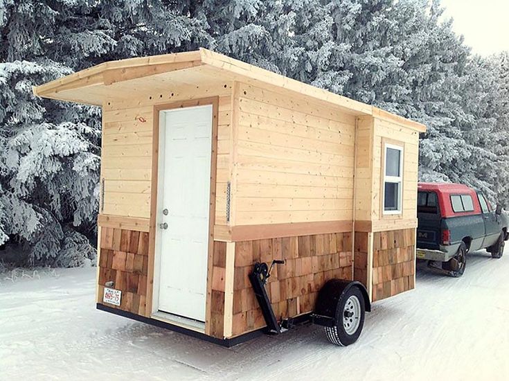 a small wooden cabin sitting in the snow next to a red truck and pine trees