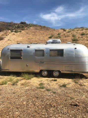 an old silver trailer parked on the side of a dirt road next to a hill