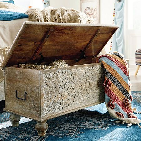 an old trunk is sitting on the floor in front of a bed with pillows and blankets