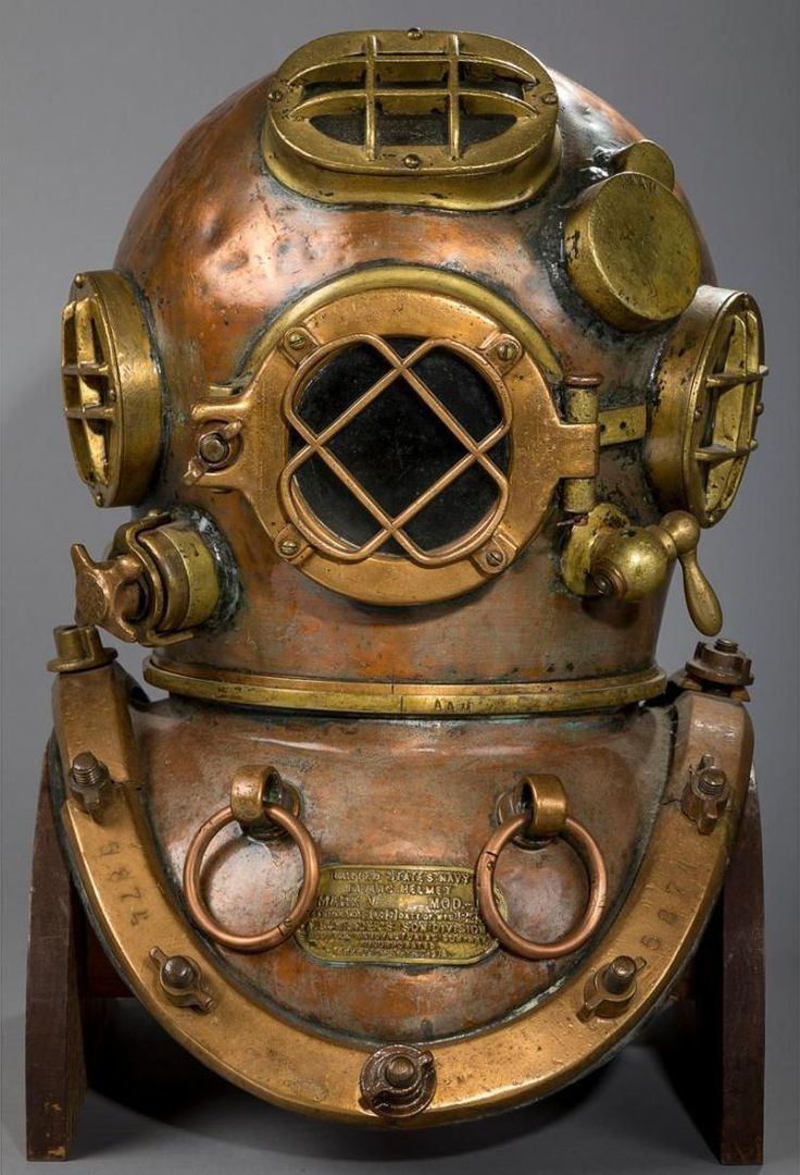 an antique diving helmet on display in front of a gray background with words below it