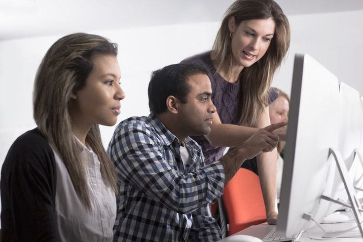 three people looking at a computer screen while another person points to something on the monitor