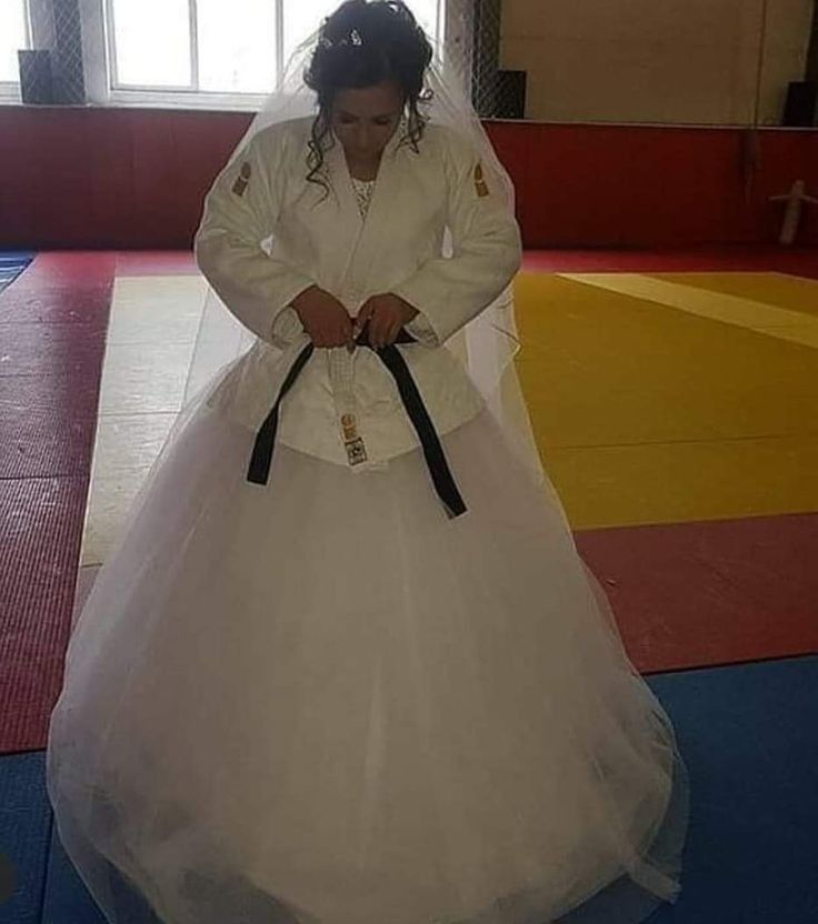 a woman in a white wedding dress standing on a blue mat with a black belt around her waist