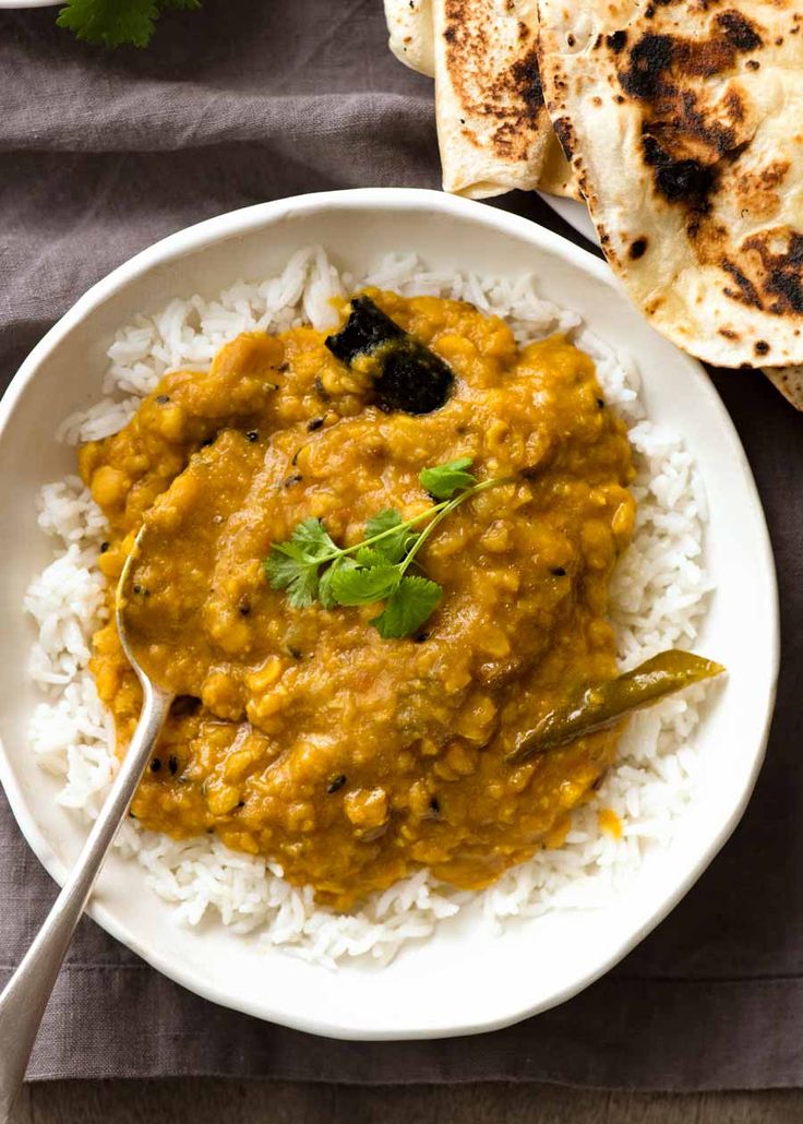 a white plate topped with rice and curry next to some pita bread on a table