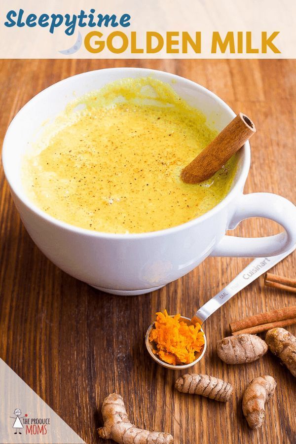 a white bowl filled with golden milk next to some ginger and cinnamon sticks on a wooden table