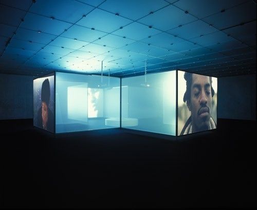 an empty room with three large screens on the wall and one man's face