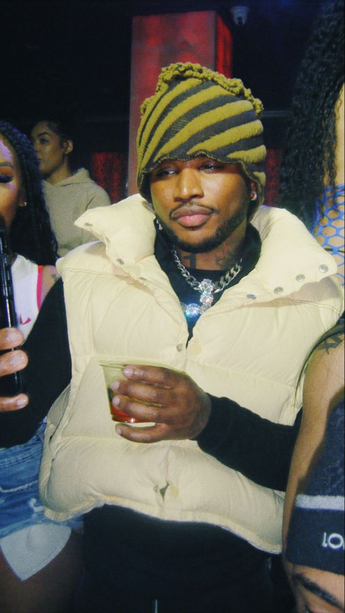 a man in a yellow jacket and hat holding a drink while looking at his cell phone