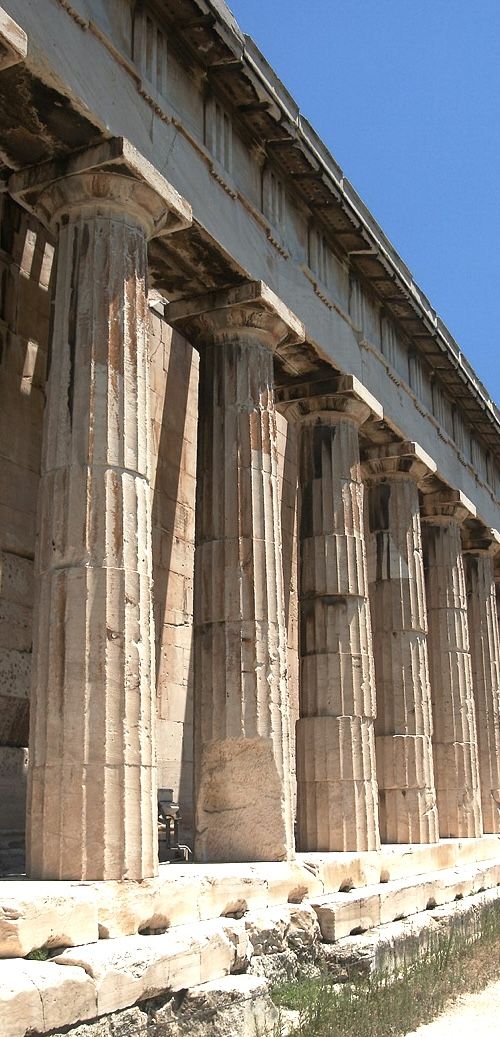 an old stone building with columns on the side and blue sky in the back ground