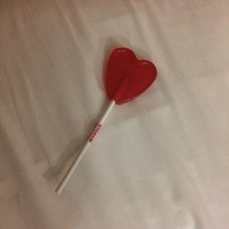 a red heart lollipop on a white sheet with a stick sticking out of it