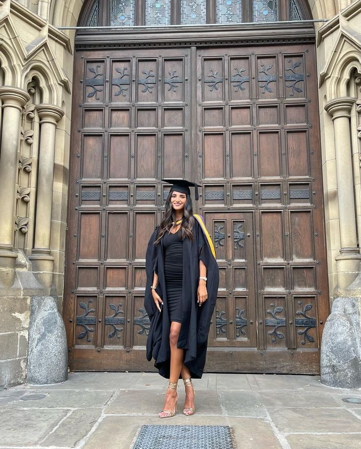 a woman standing in front of a large wooden door wearing a graduation cap and gown