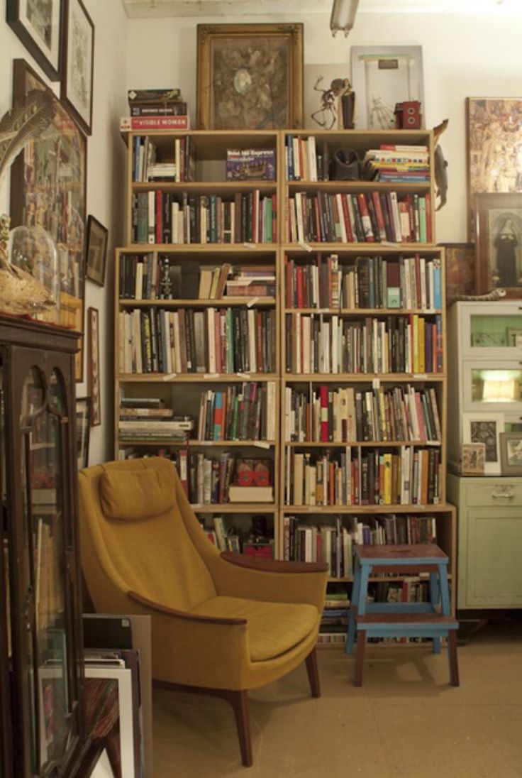 a living room filled with lots of books on top of a wooden shelf next to a yellow chair