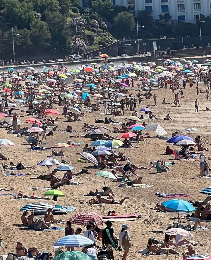 many people are laying on the beach with their umbrellas up in the air,