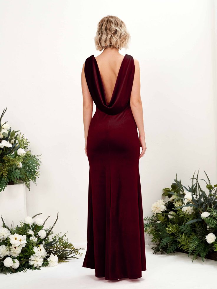 the back of a woman in a brown dress standing next to flowers and greenery