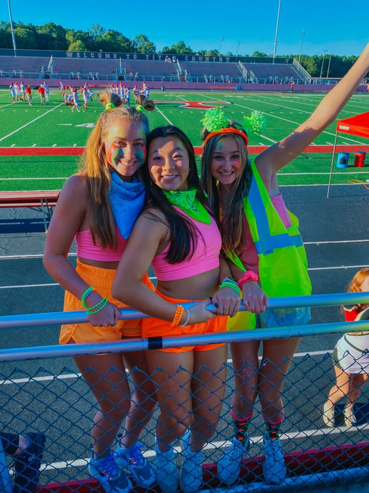 three girls are posing for the camera in front of a fence at a sports field