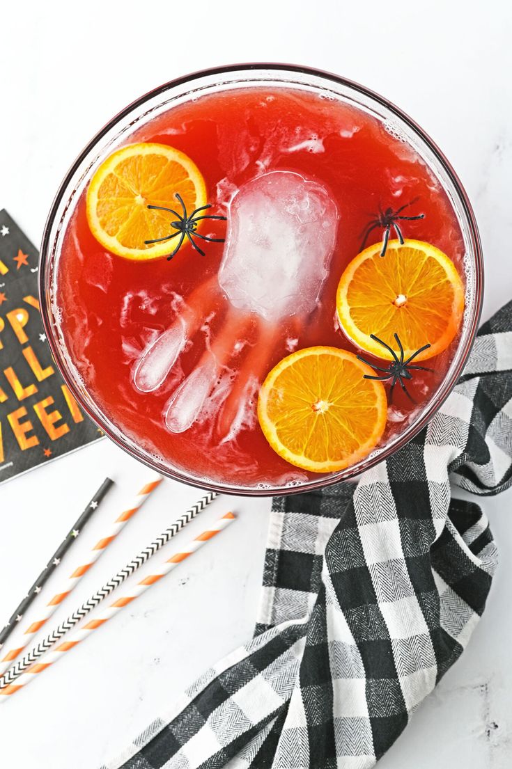 a drink in a glass with orange slices and spider webs on the rim, next to halloween decorations