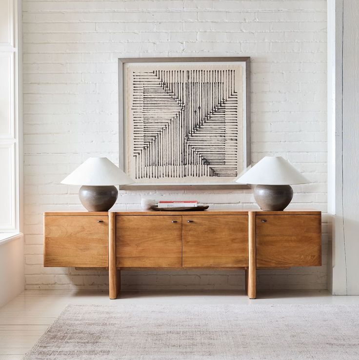 two lamps sitting on top of a wooden cabinet in front of a white brick wall