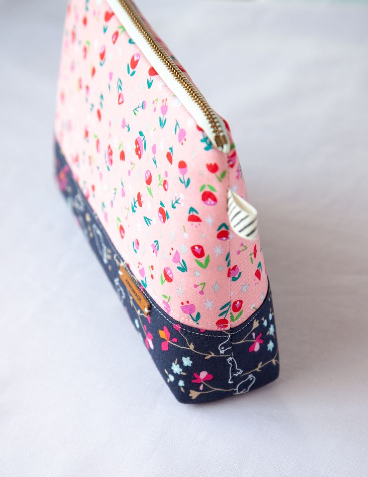 a small pink and blue purse with flowers on it's front pocket, sitting on a white surface