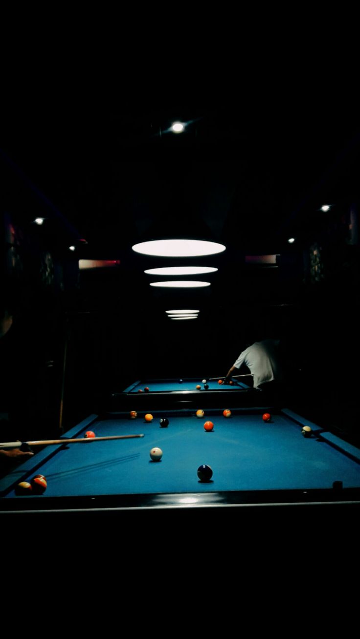 a pool table in the dark with balls on it and a person leaning over to take a shot