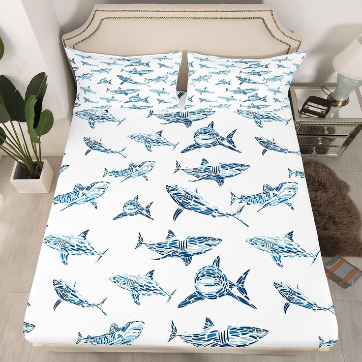 a bed covered in blue and white sharks on it's side, next to a plant