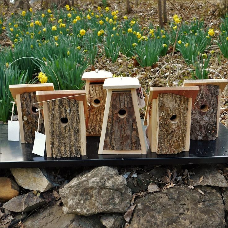 four wooden birdhouses sitting on top of a black shelf next to rocks and flowers