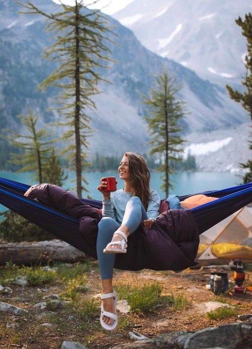 a woman is sitting in a hammock with her feet up and holding a cup