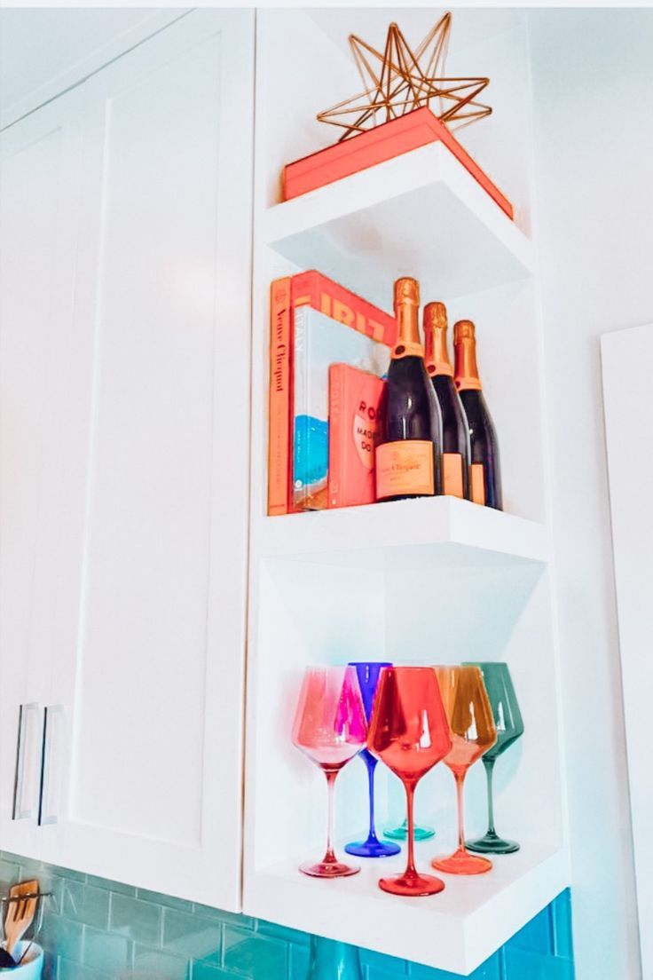 wine glasses and bottles are sitting on the shelves in this white kitchen cupboards,