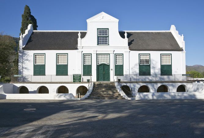 an old white house with green shutters on the front and stairs leading up to it