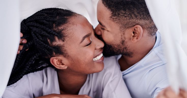 a man and woman laying in bed under a white sheet smiling at each other with their eyes closed