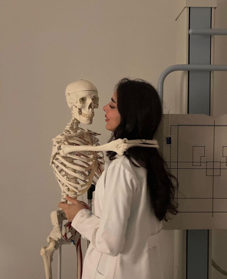 a woman standing next to a skeleton in a white lab coat looking at it's back