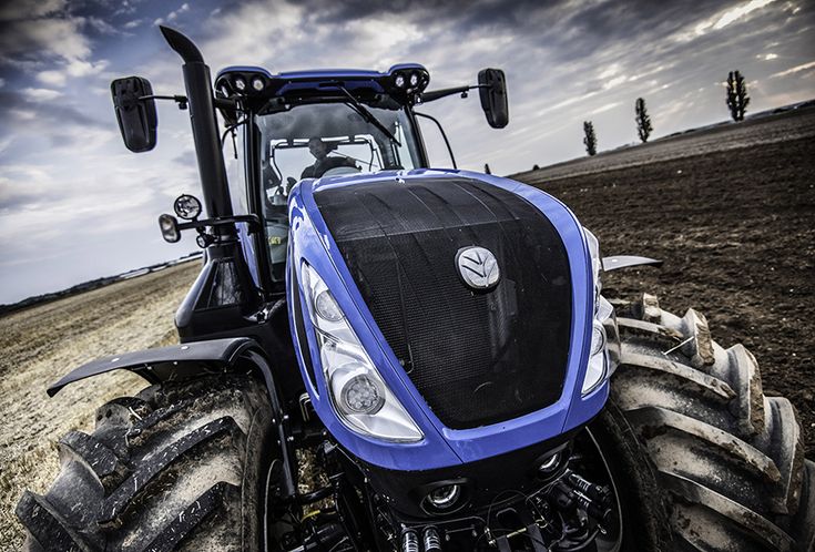 a blue tractor parked on the side of a dirt road in front of a cloudy sky