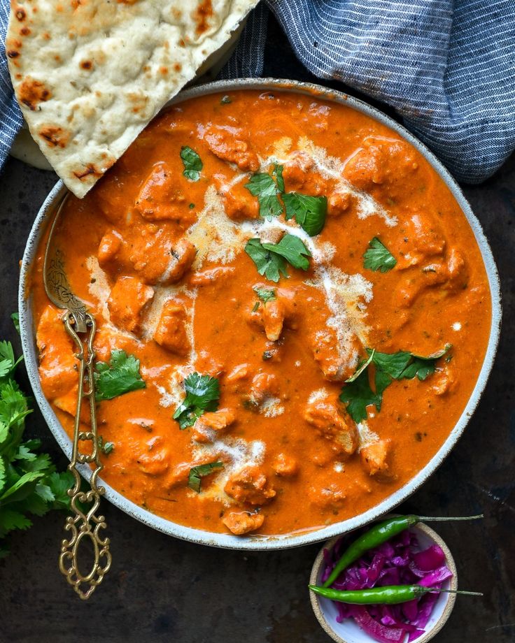 an overhead view of a bowl of chicken tikka with pita bread on the side