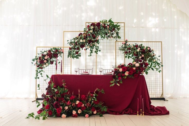 the table is covered with red and pink flowers, greenery and candles on it