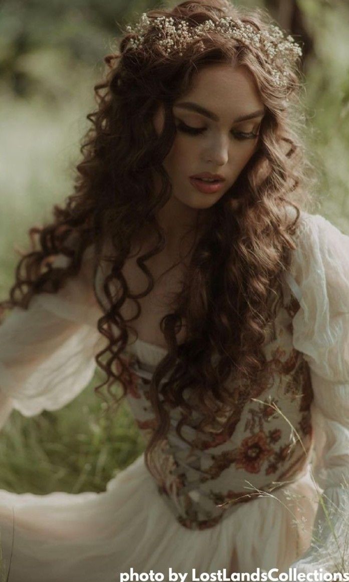 a woman with long hair wearing a white dress sitting on the ground in tall grass