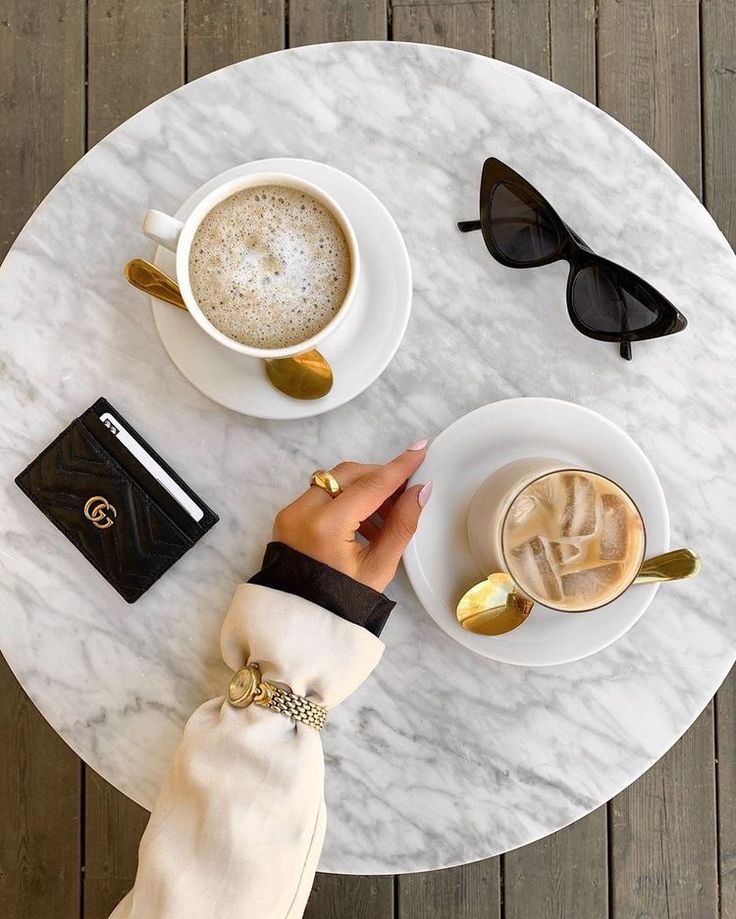 a person is sitting at a table with two cups of coffee and a book on it