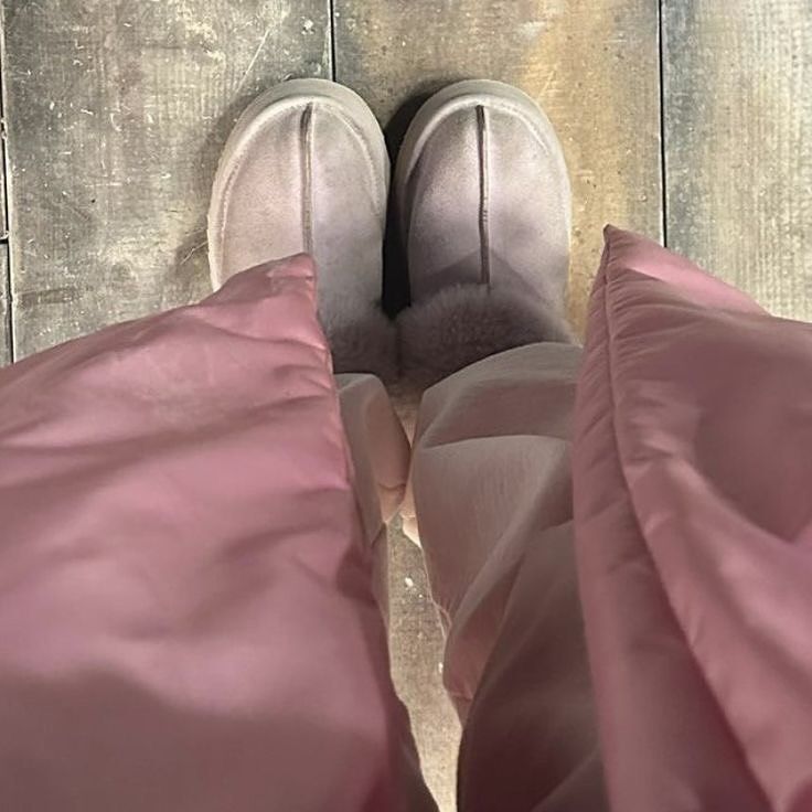 a person's feet in slippers standing on a wooden floor with pink sheets