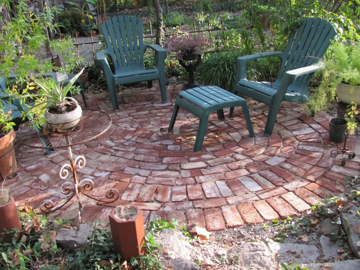 two green chairs sitting on top of a brick patio surrounded by potted plants and greenery