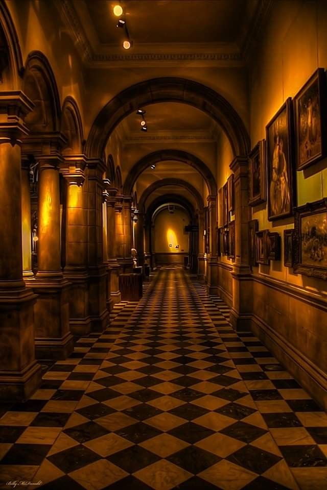 an empty hallway with paintings on the walls and checkered flooring in black and white