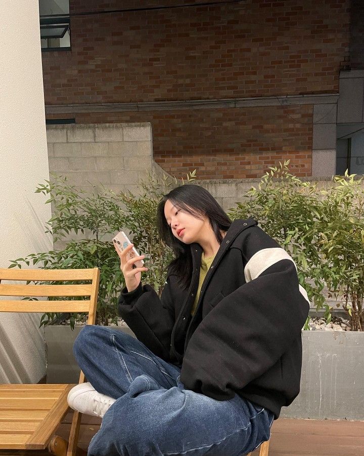 a woman sitting on a wooden bench looking at her cell phone while she sits down