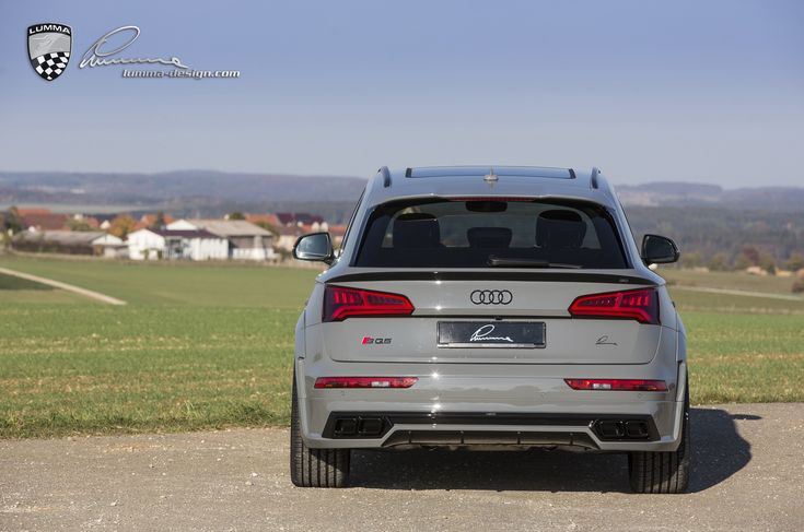 the rear end of an audi car parked on a road in front of a field