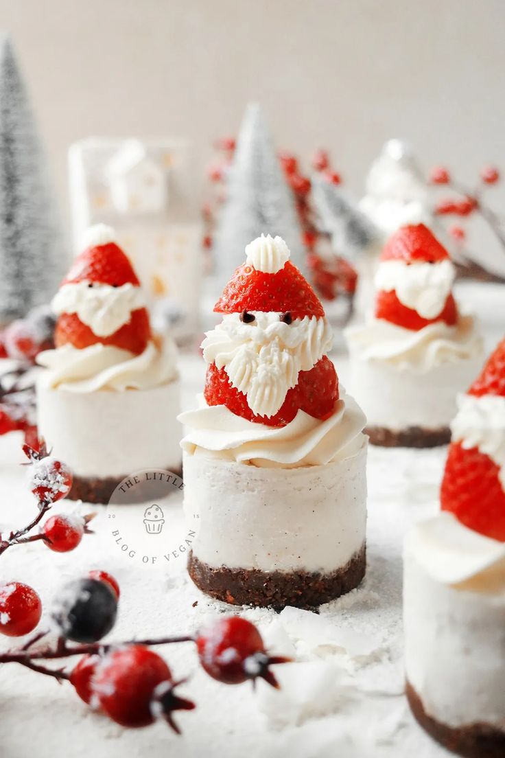 mini cheesecakes decorated with whipped cream and strawberries are displayed on a table