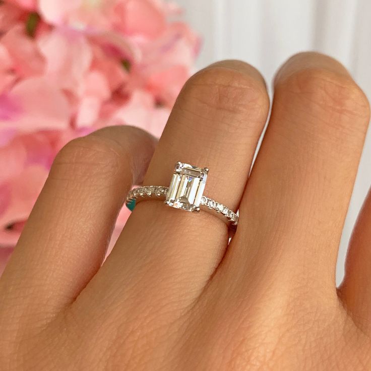 a woman's hand with a diamond ring on it and pink flowers in the background